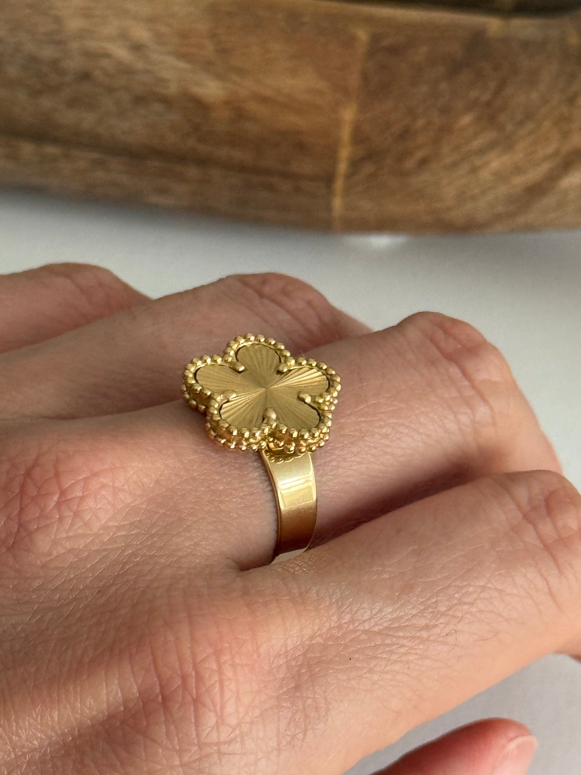 Gold ring with flower design on a hand against a wooden background