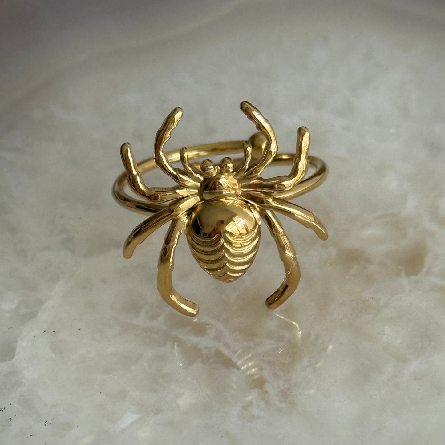 Gold crab-shaped ring on a light stone surface