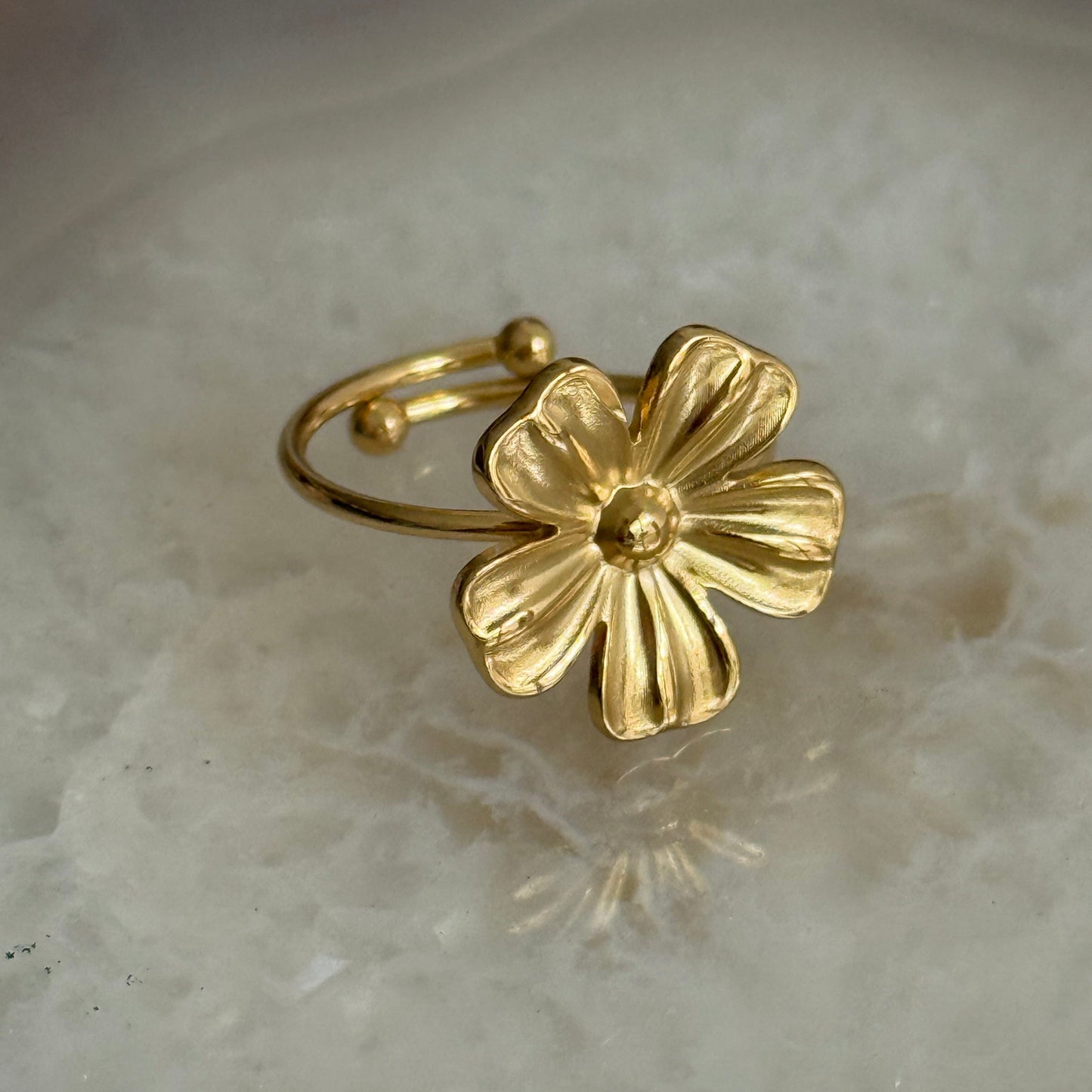 Gold flower-shaped ring on a light stone surface