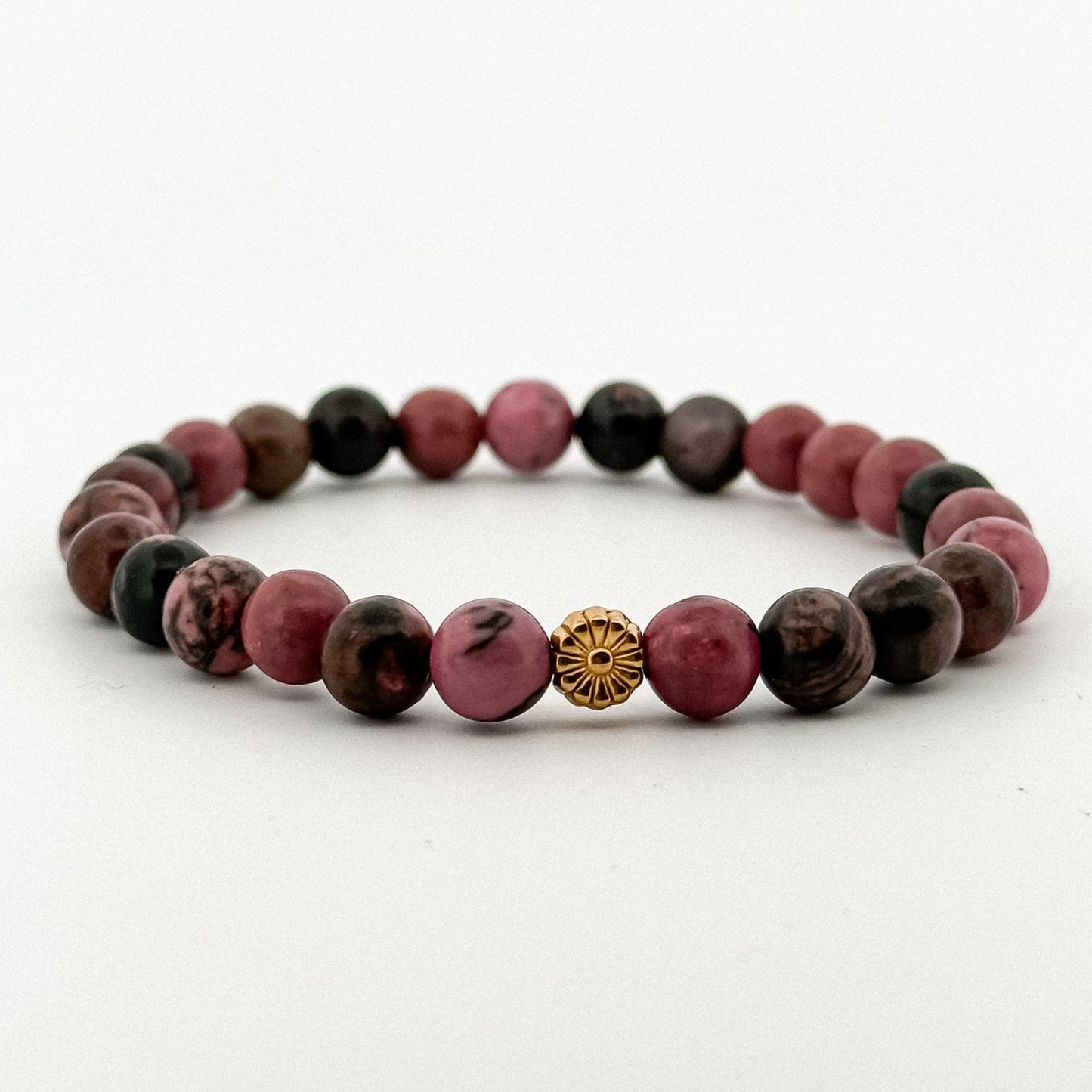 Beaded bracelet with pink and brown beads and a gold center piece on a white background