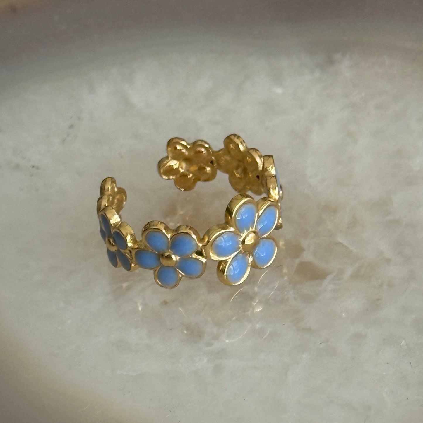 Gold ring with blue flower-shaped stones on a light background