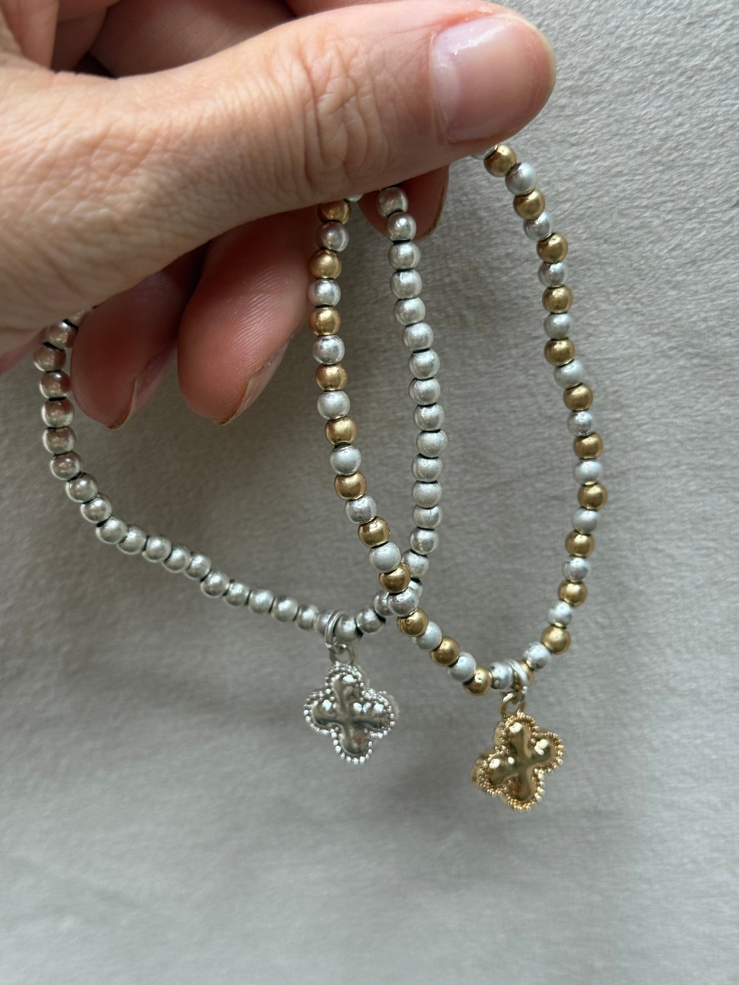 Two beaded bracelets with clover charms held by a hand on a neutral background
