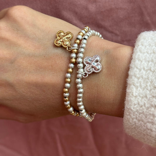 Two pearl bracelets with heart-shaped charms on a wrist against a pink background