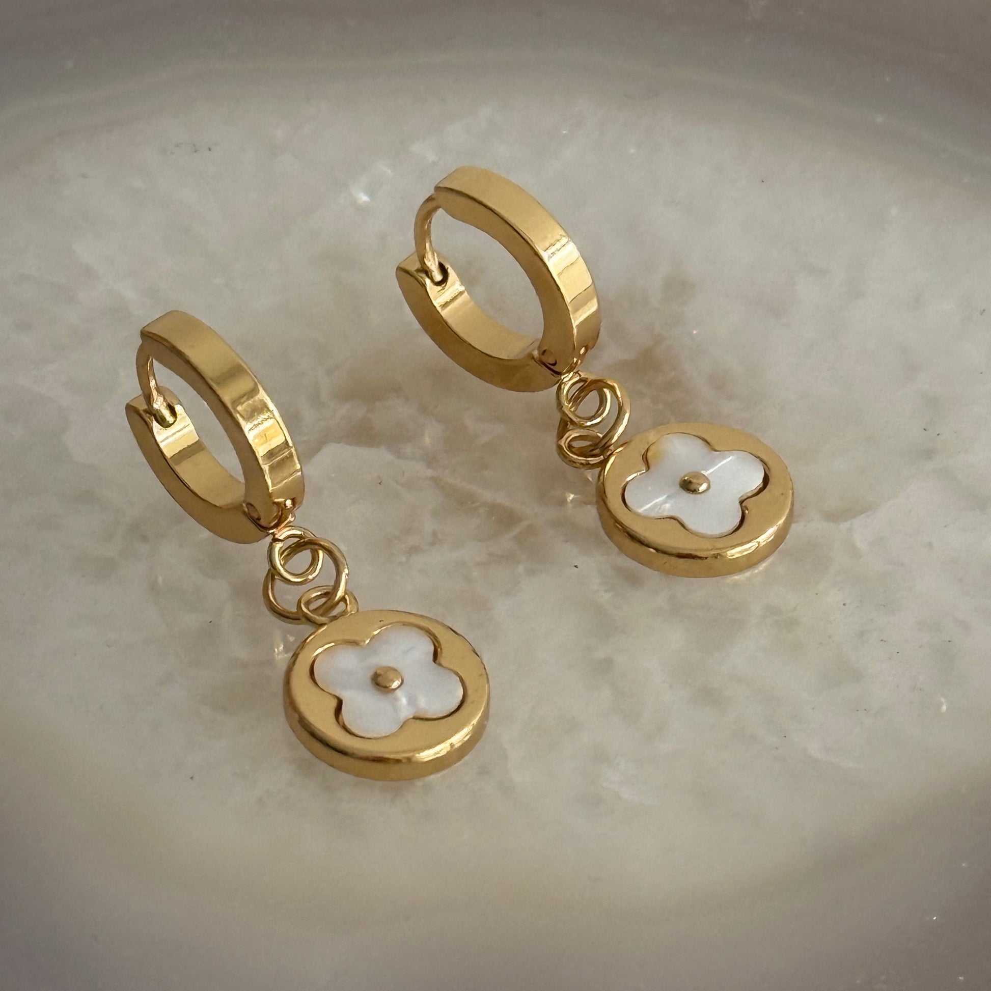 Gold hoop earrings with floral charms on a marble surface