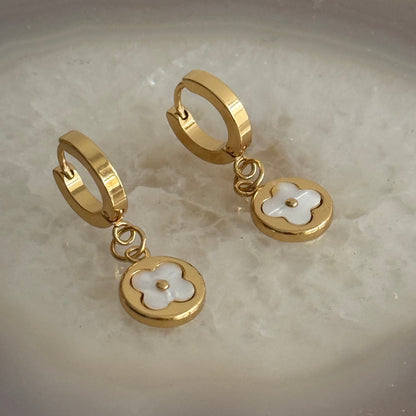 Gold hoop earrings with floral charms on a marble surface
