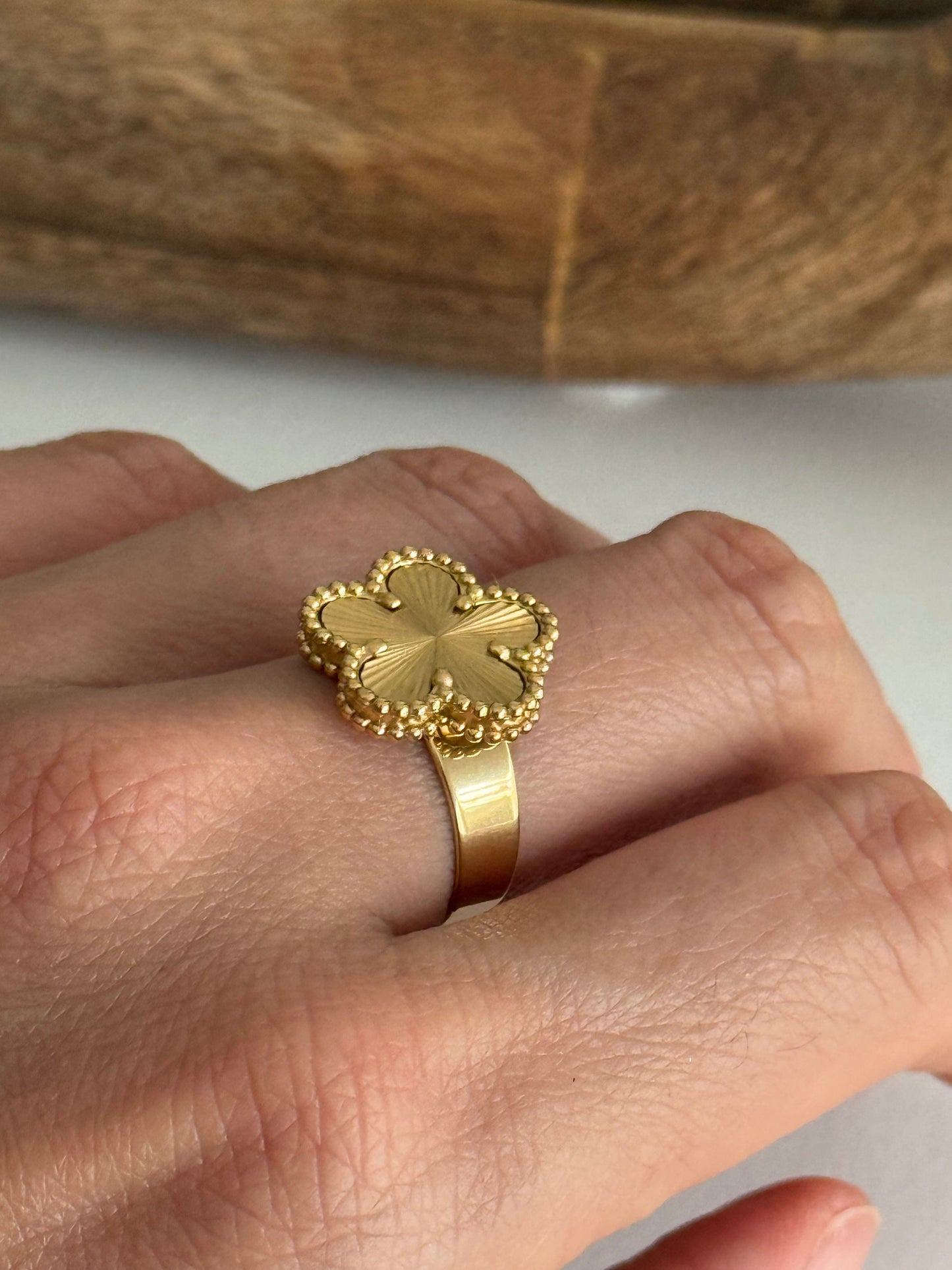 Gold ring with flower design on a hand against a wooden background