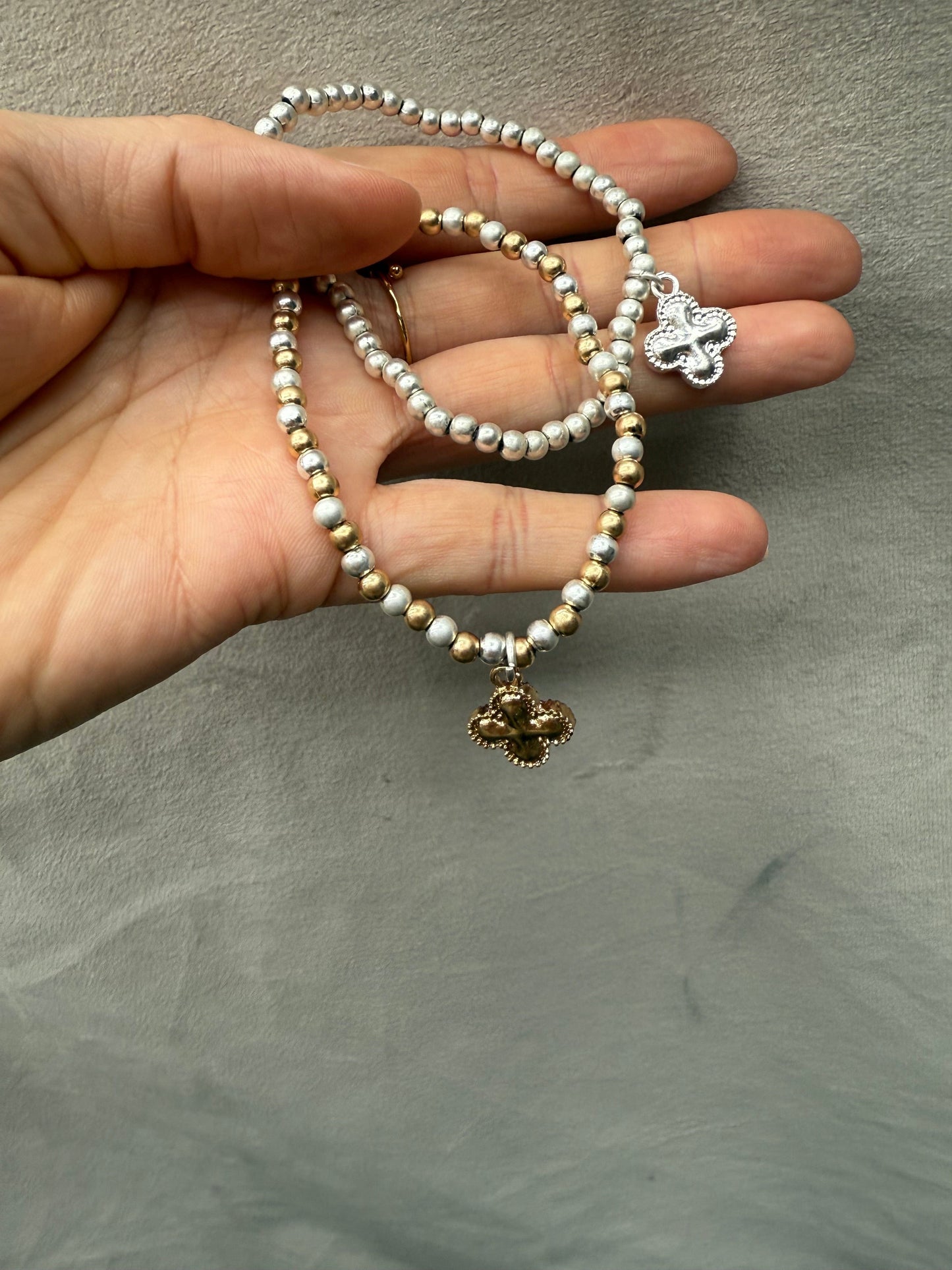 Hand holding two pearl bracelets with charms against a neutral background