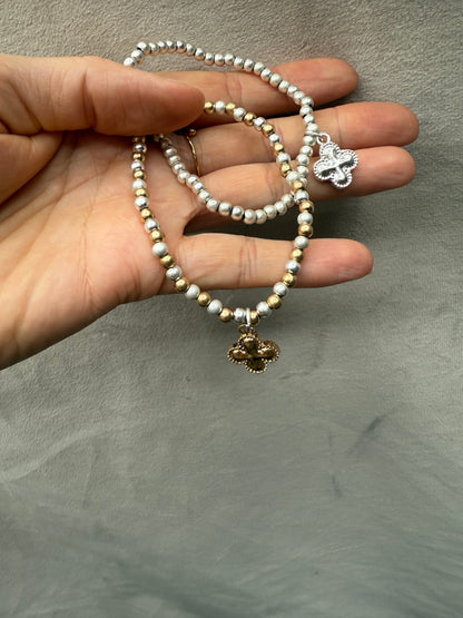 Hand holding two pearl bracelets with charms against a neutral background