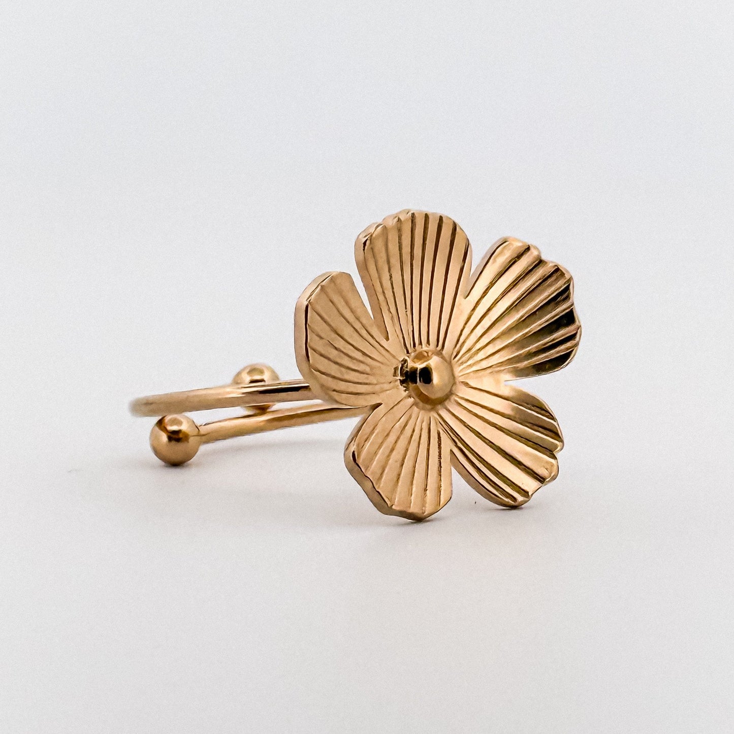 Gold flower-shaped ring on a light gray background