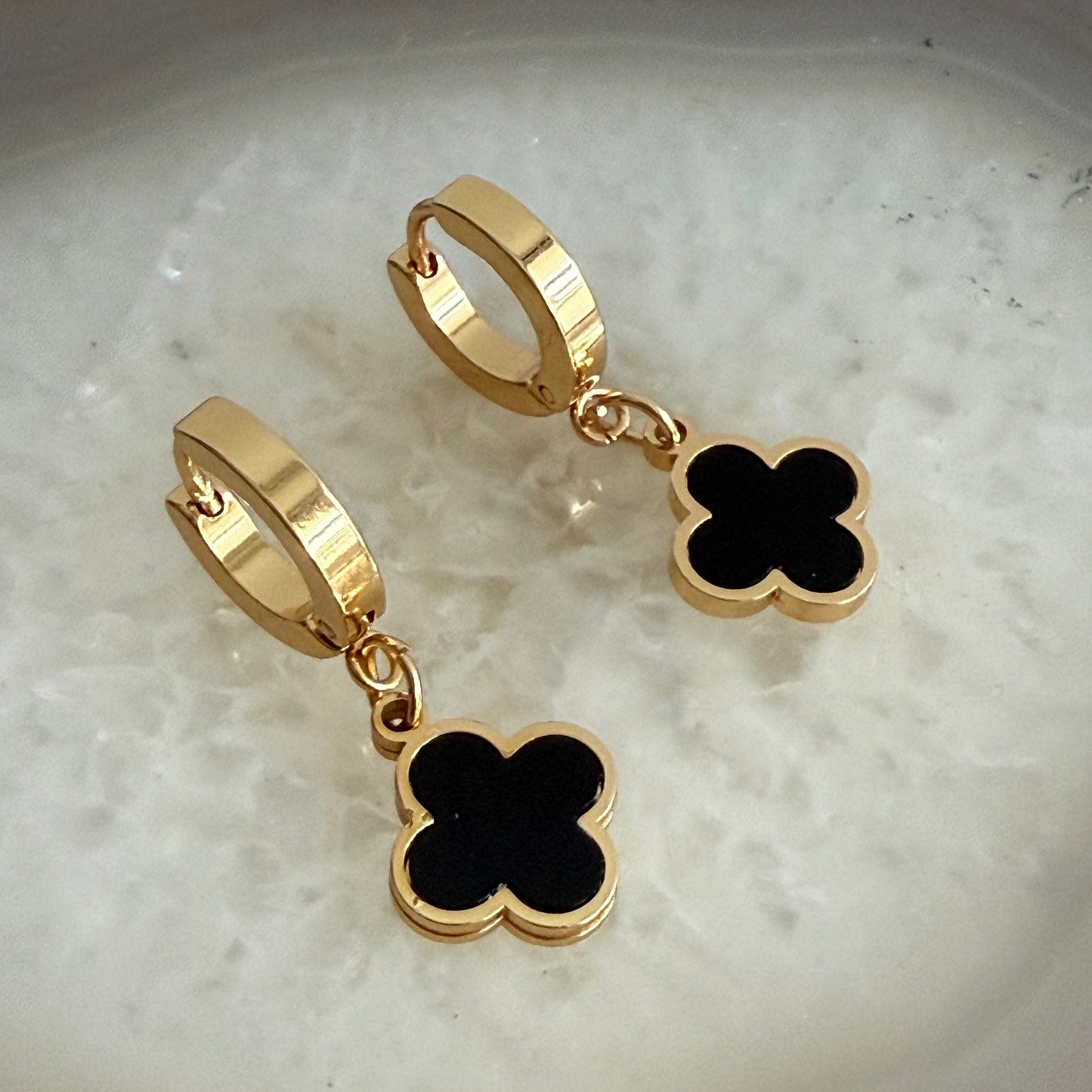 Gold hoop earrings with black clover-shaped charms on a light background
