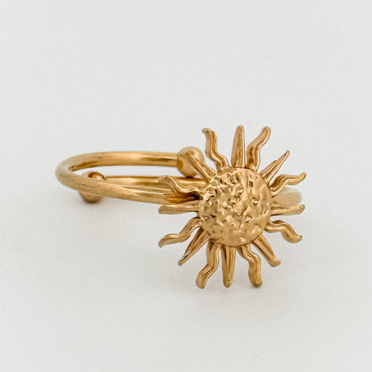 Gold sun-shaped ring on a light gray background