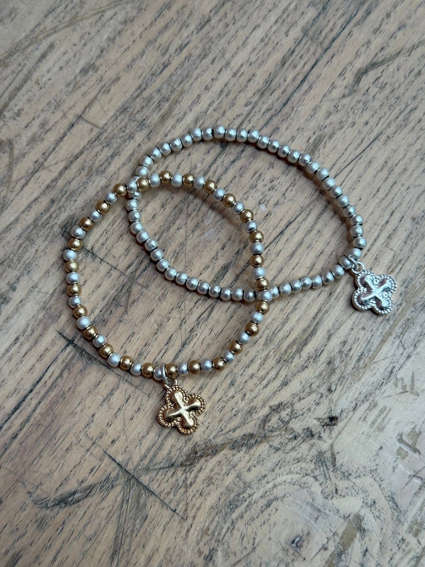 Set of Two beaded bracelets with clover-shaped pendants on a wooden surface