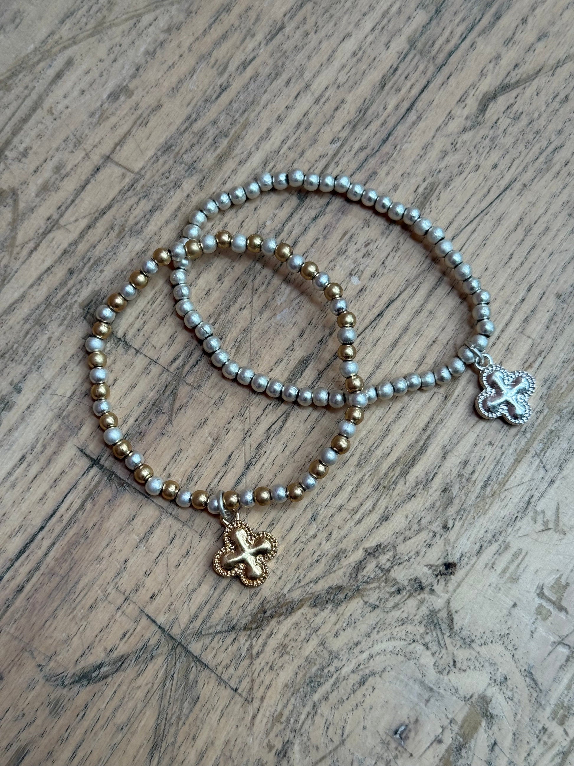 Set of Two beaded bracelets with clover-shaped pendants on a wooden surface