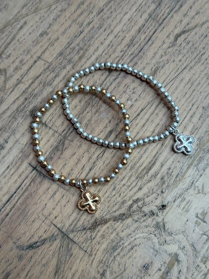 Set of Two beaded bracelets with clover-shaped pendants on a wooden surface