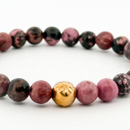 Bracelet with pink and black beads and a gold accent bead on a white background