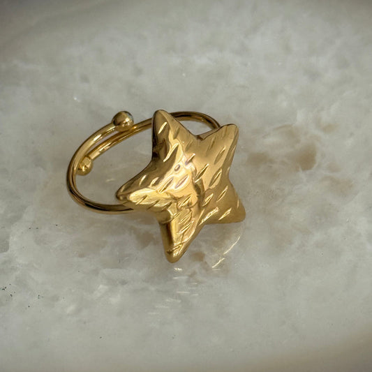 Gold star-shaped ring on a light marble background
