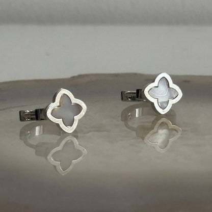 Silver clover-shaped earrings on a reflective surface with a neutral background