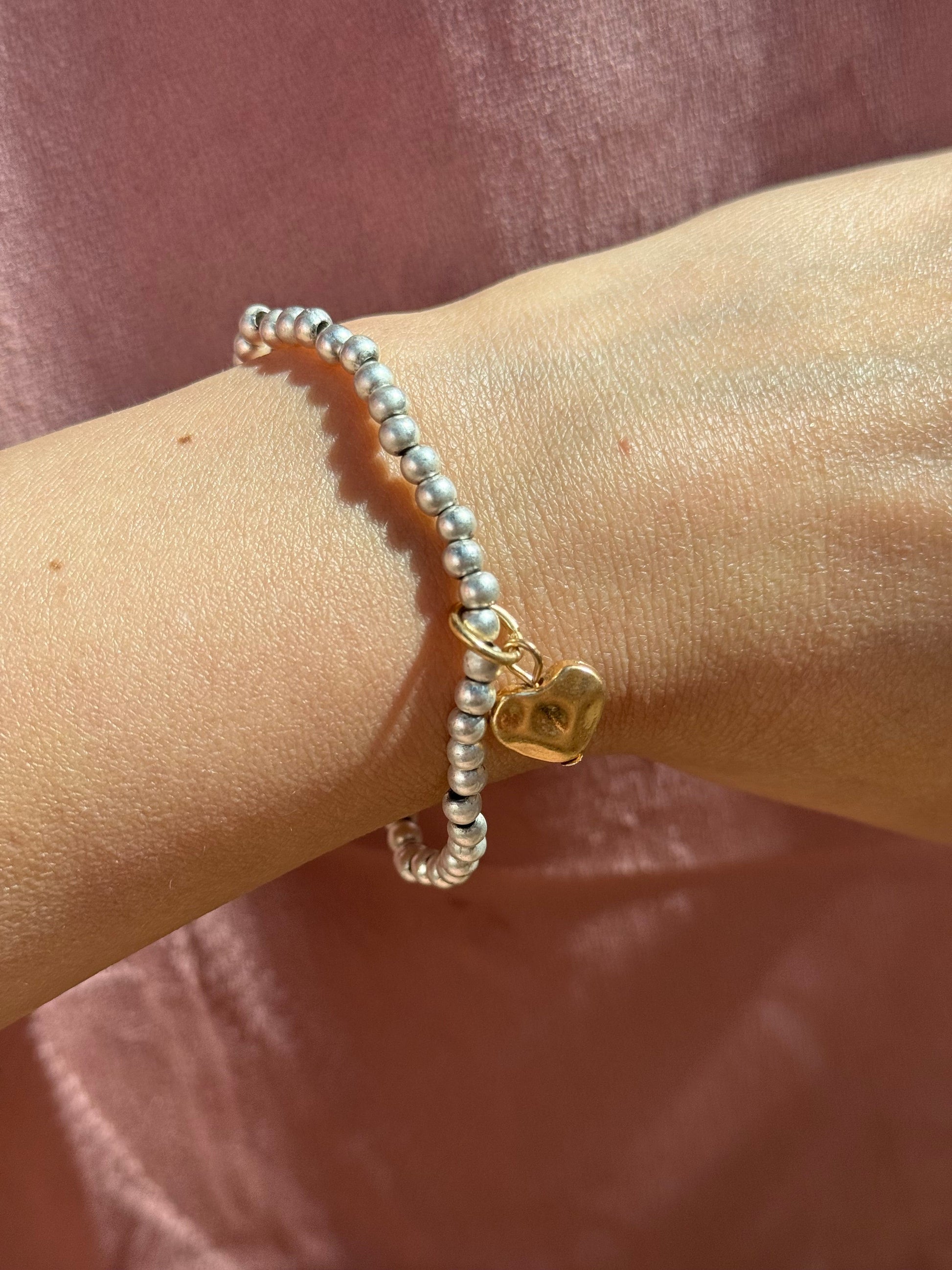 Silver bead bracelet with a gold heart charm on a wrist