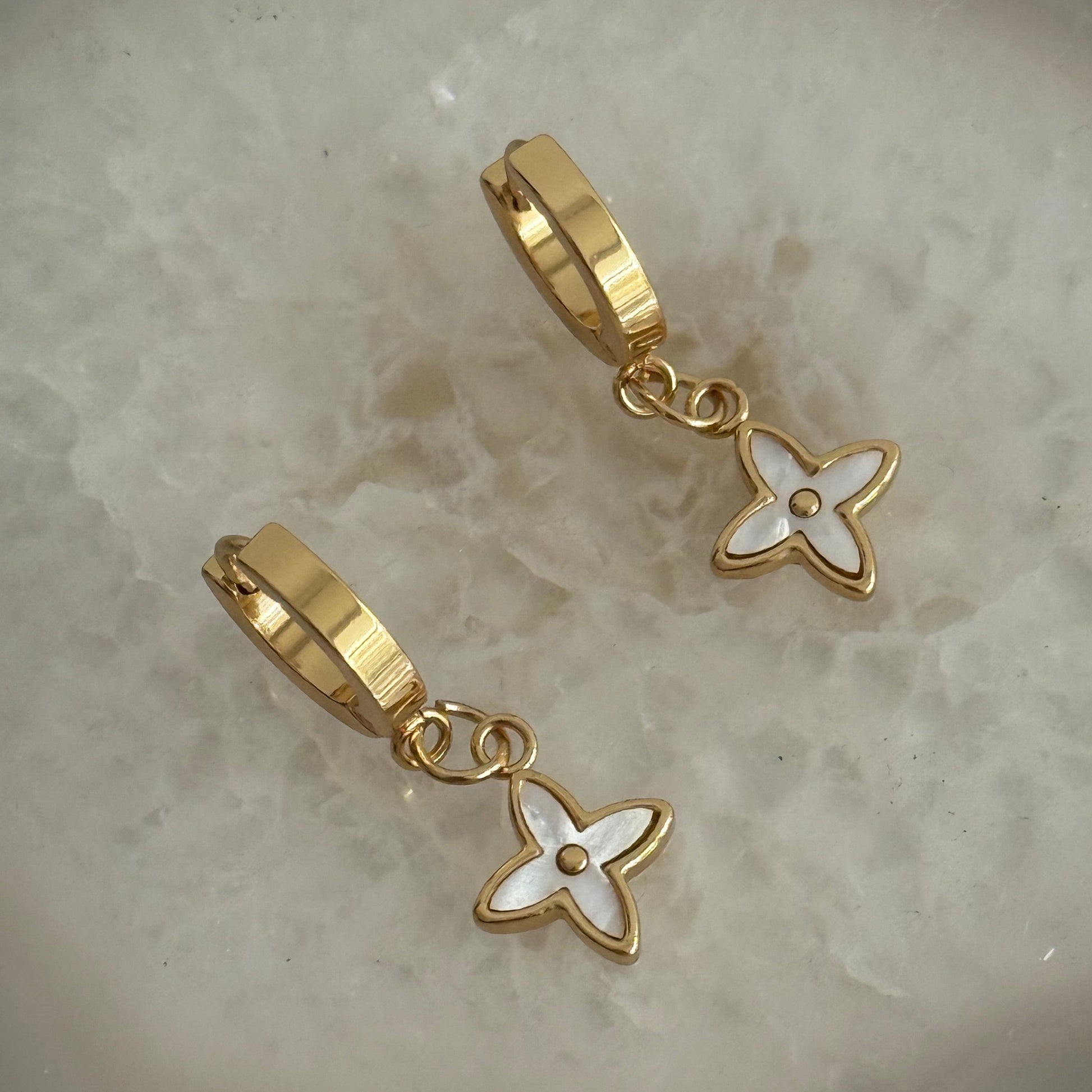 Gold earrings with floral designs on a textured surface