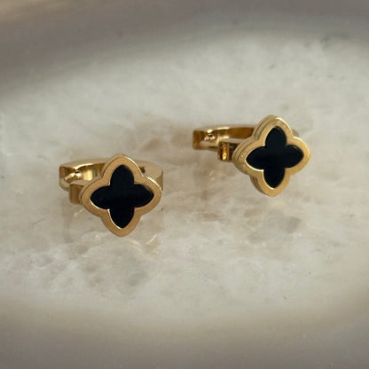 Gold and black clover-shaped earrings on a marble surface