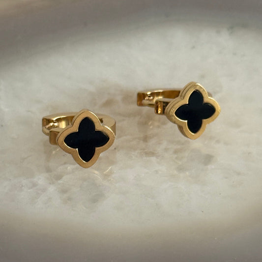 Gold and black clover-shaped earrings on a marble surface
