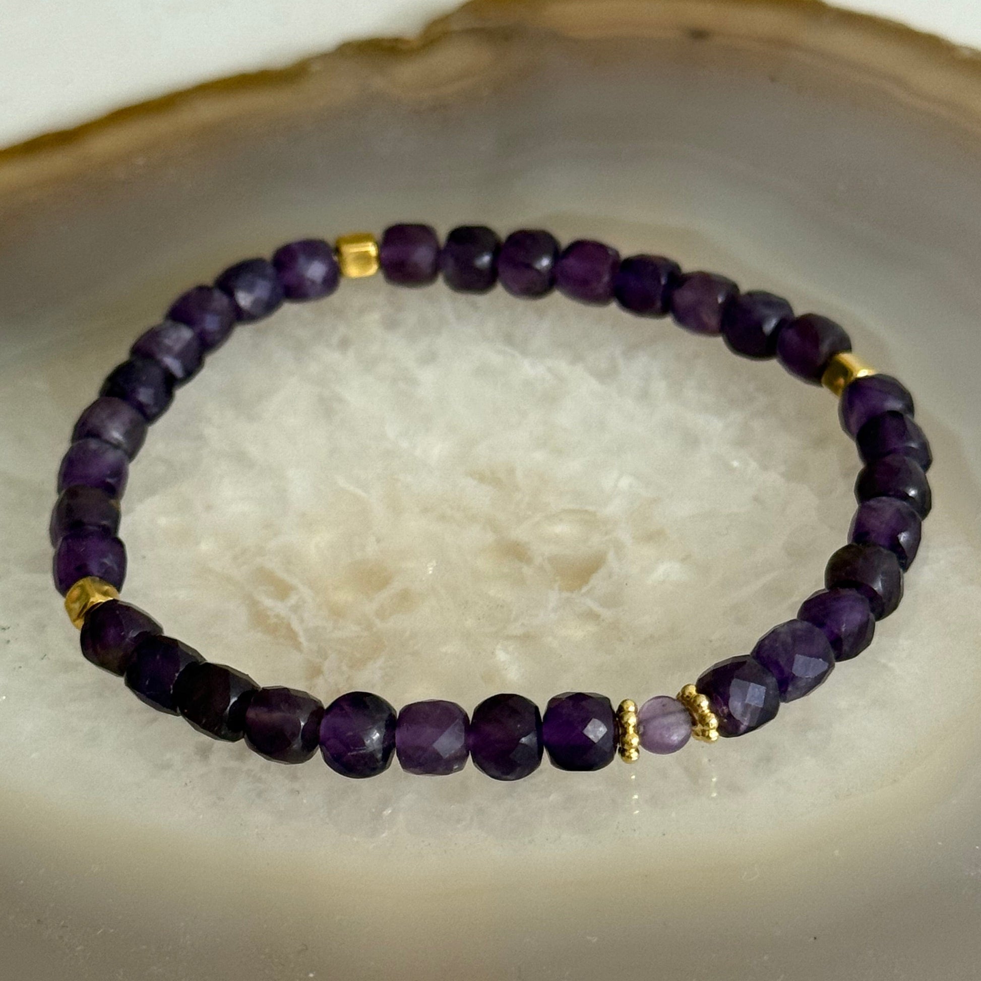 Purple beaded bracelet with gold accents on a textured white surface