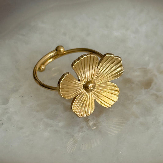 Gold floral ring on a textured beige surface