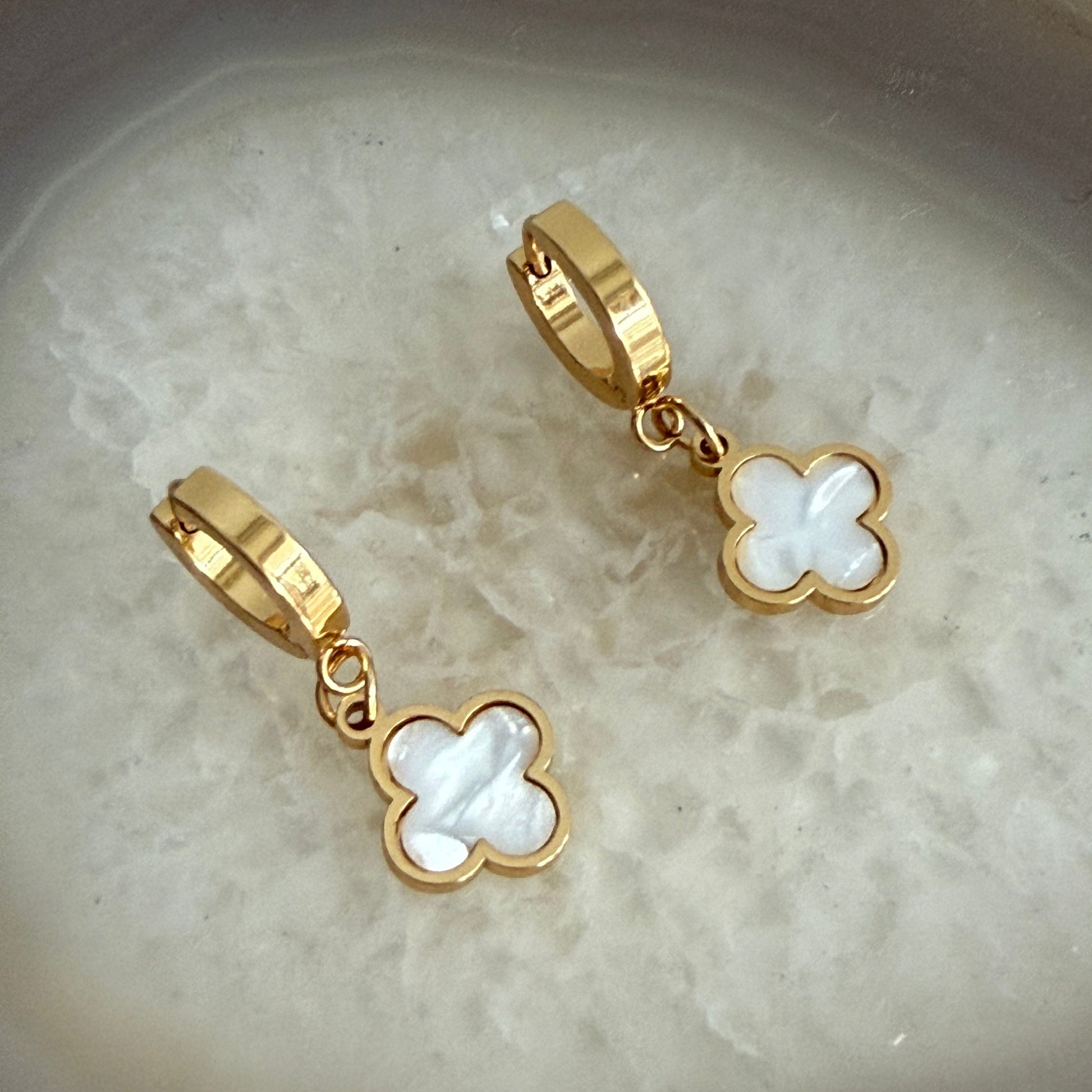 Gold and white clover-shaped earrings on a textured beige surface