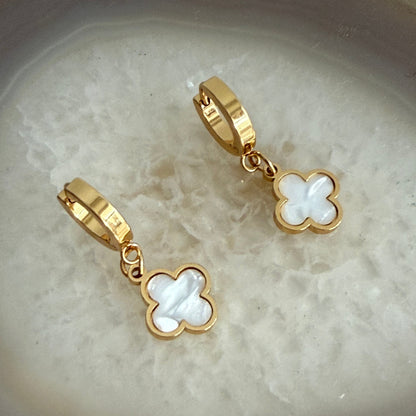 Gold and white clover-shaped earrings on a textured beige surface