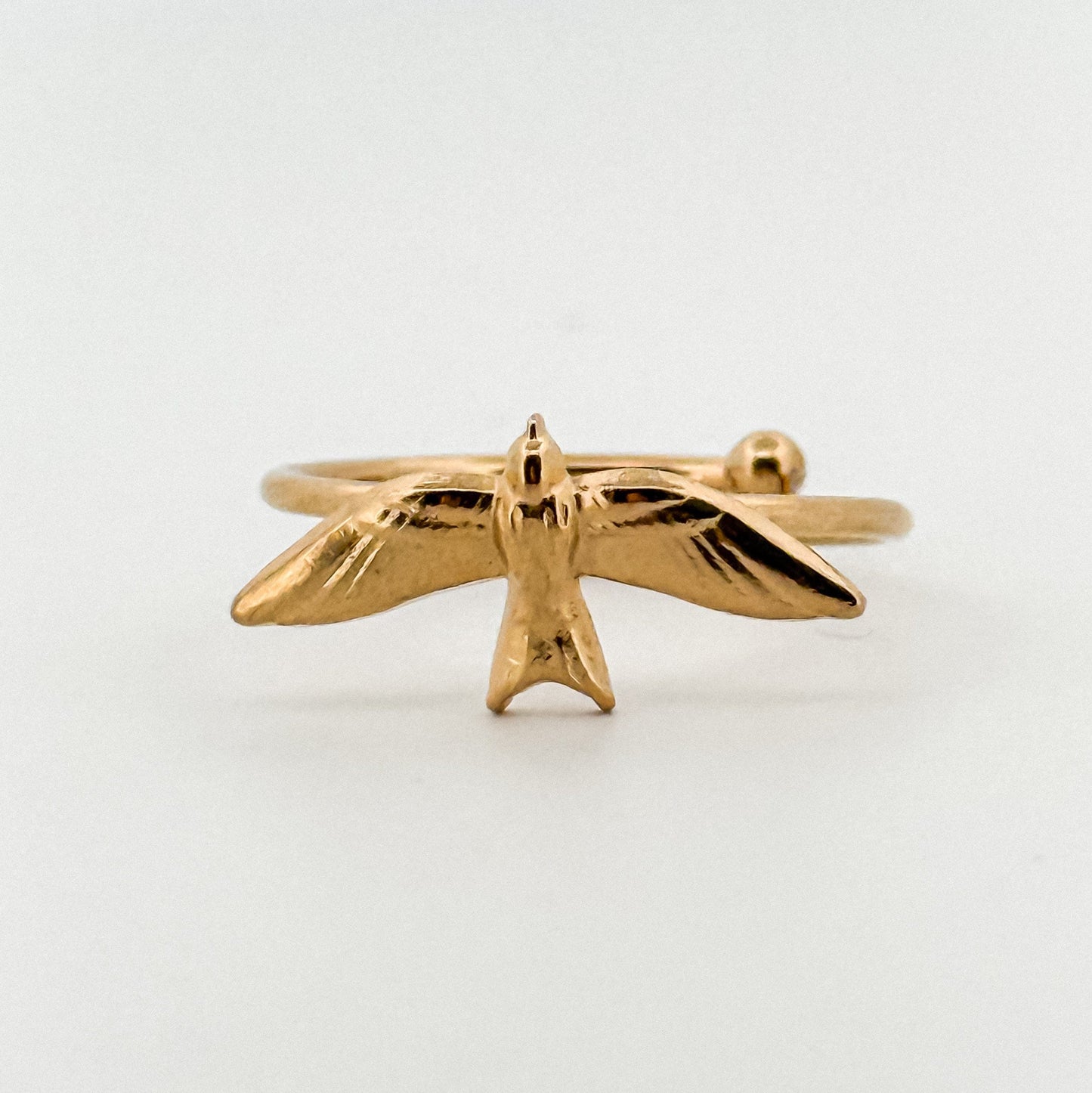 Gold bird-shaped ring on a light background