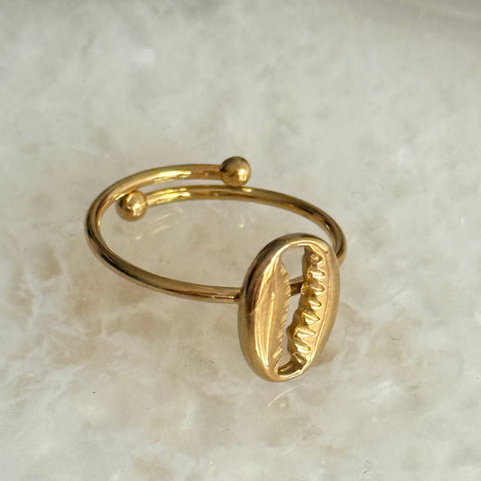 Gold ring with a cowrie shell design on a light marble background