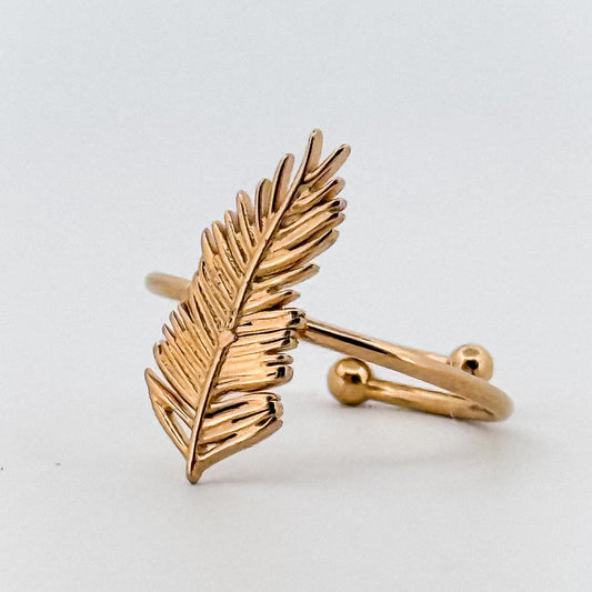 Gold feather-shaped ring on a light gray background