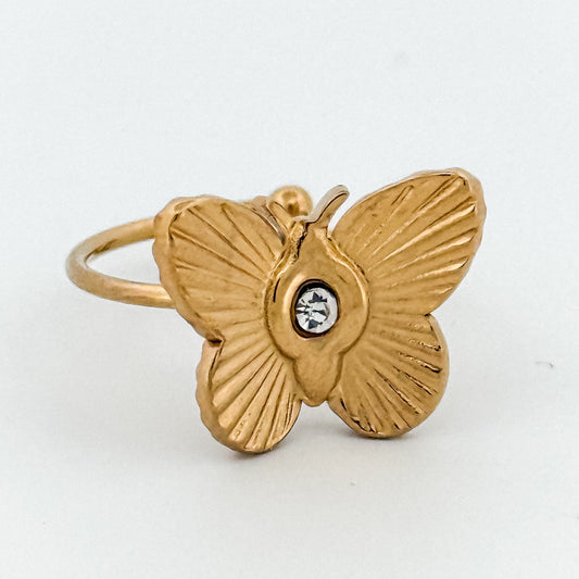 Gold butterfly ring with a central gemstone on a white background