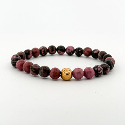 Bracelet with purple and black beads and a gold charm on a white background