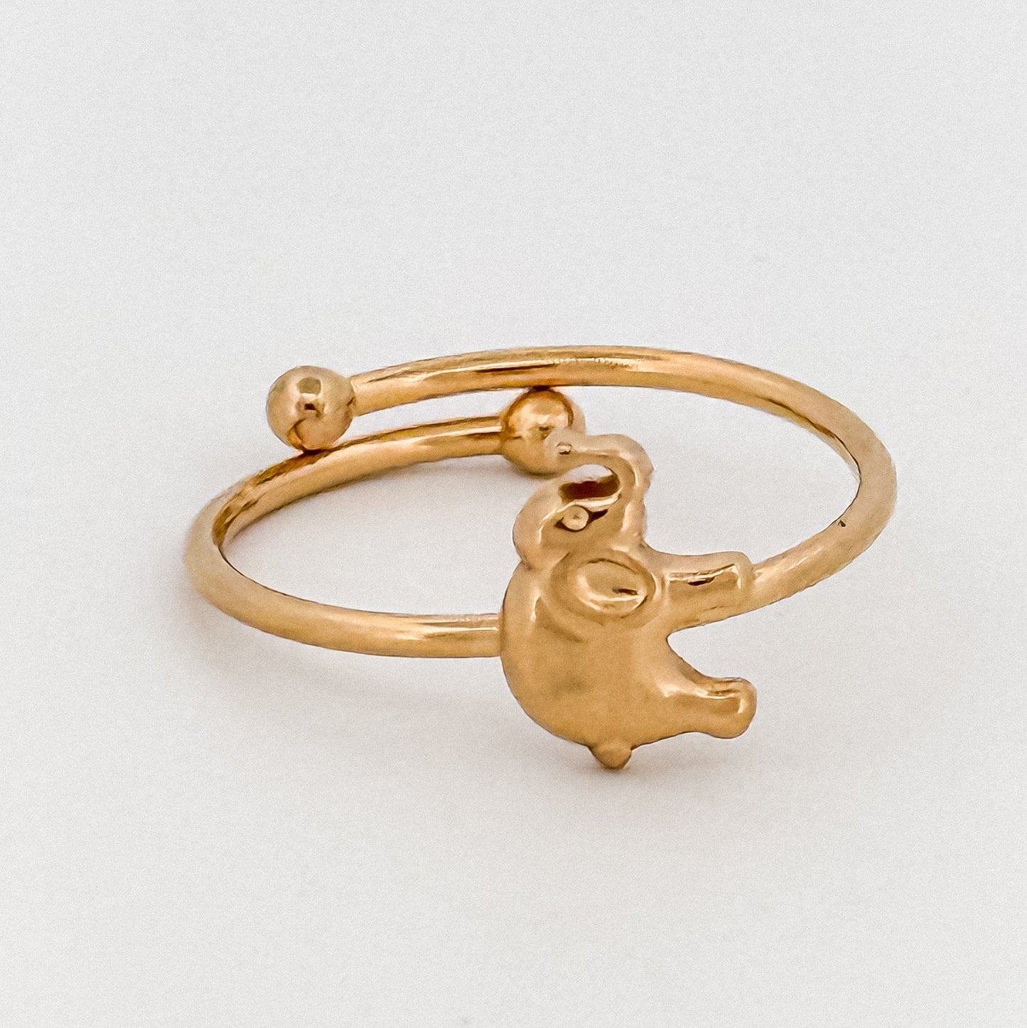 Gold ring with a small elephant charm on a light gray background
