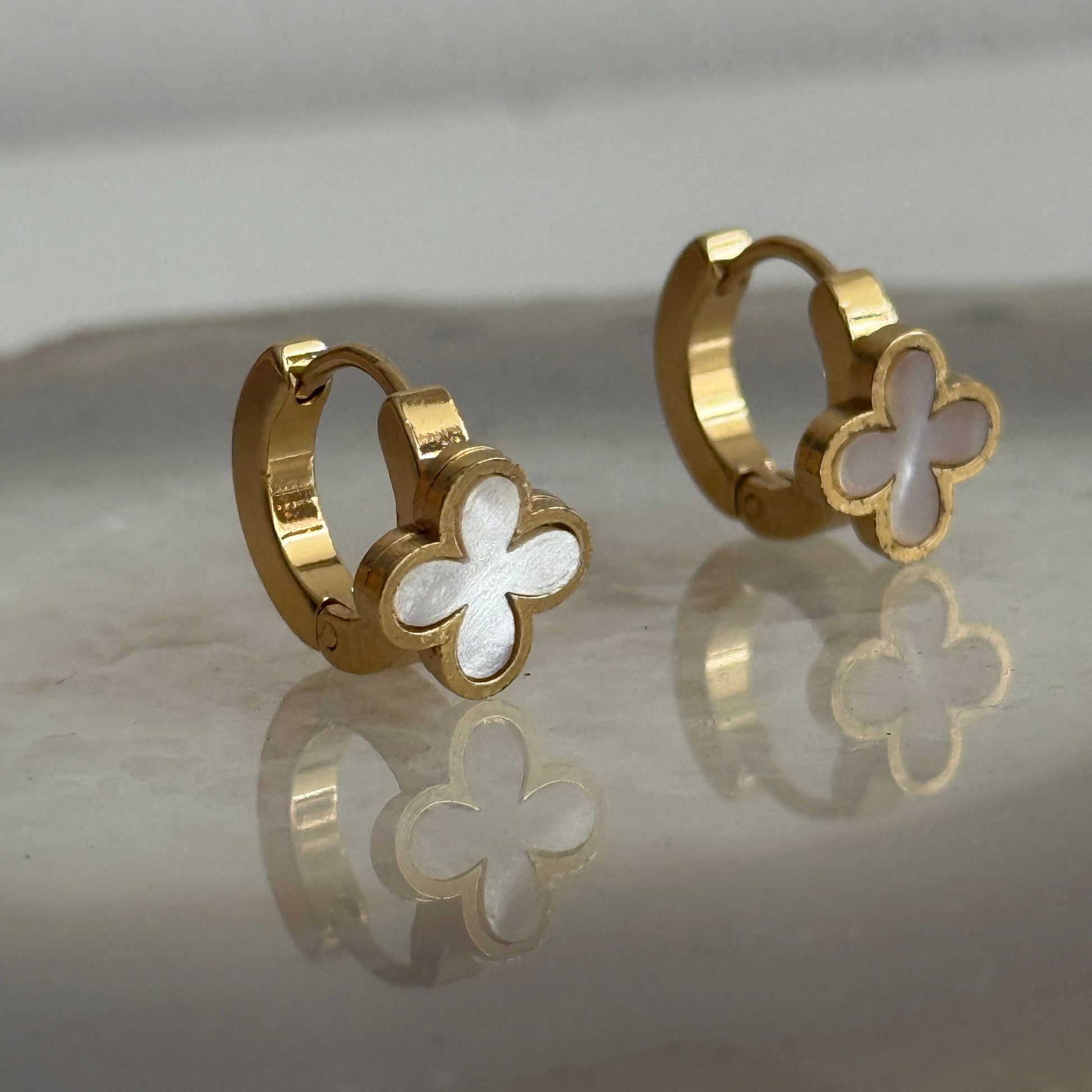 Gold hoop earrings with clover-shaped ends on a reflective surface