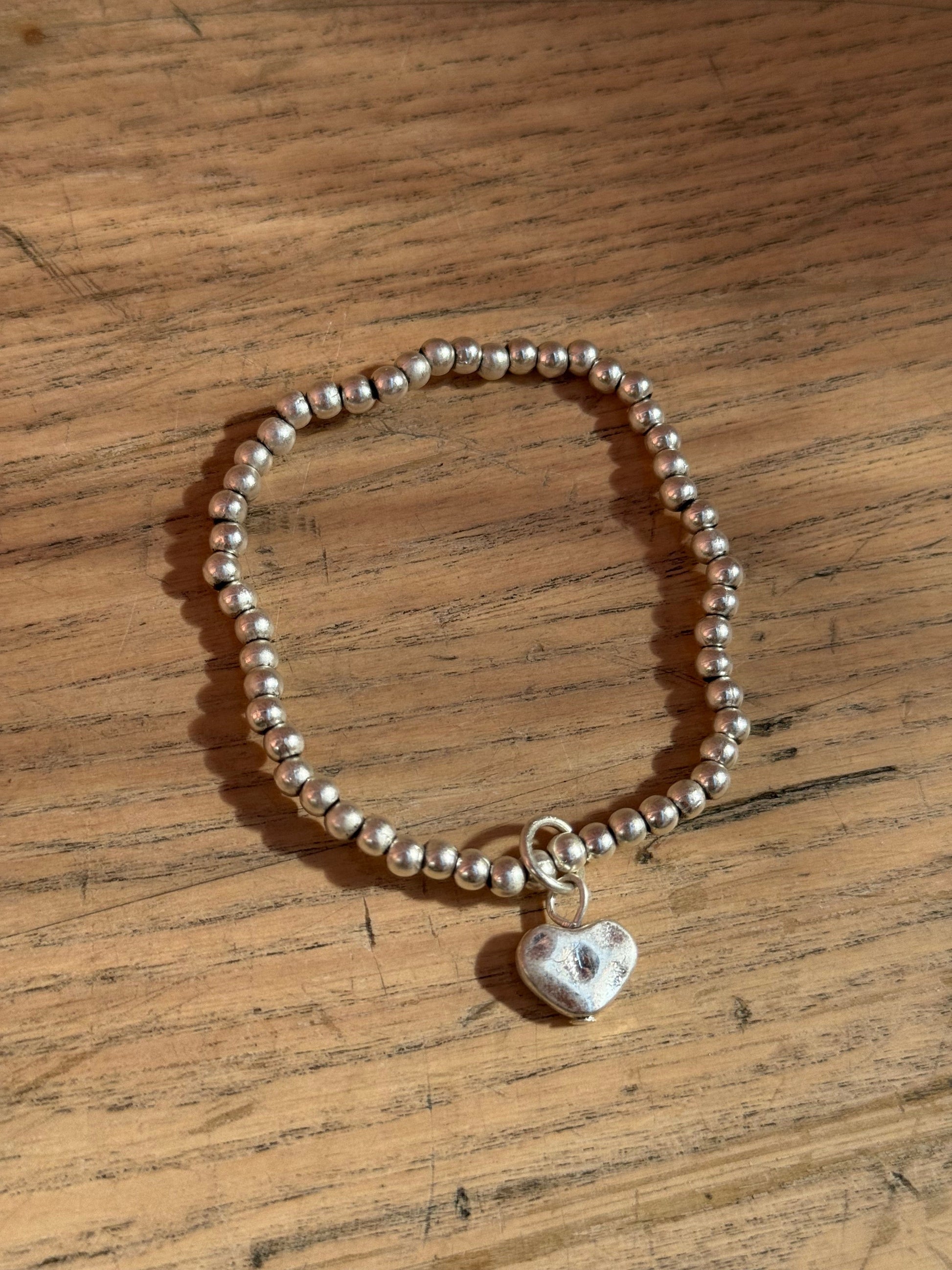 Silver bracelet with a heart charm on a wooden surface