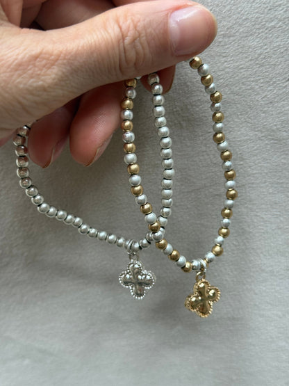 Two beaded bracelets with clover charms held by a hand on a neutral background
