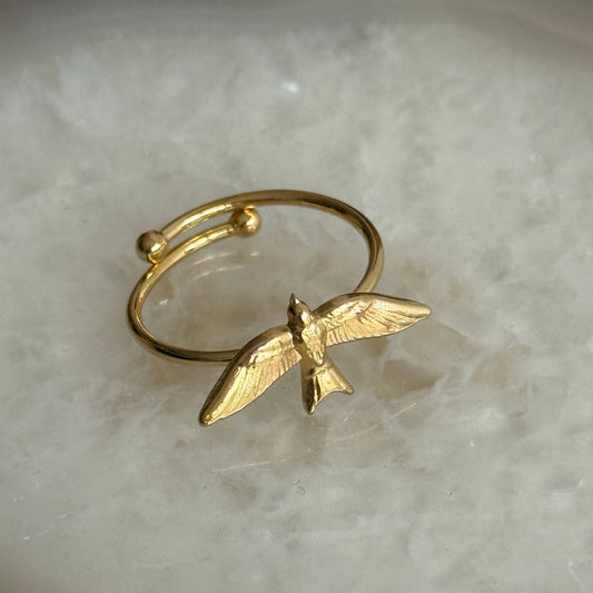 Gold bird-shaped ring on a light stone background