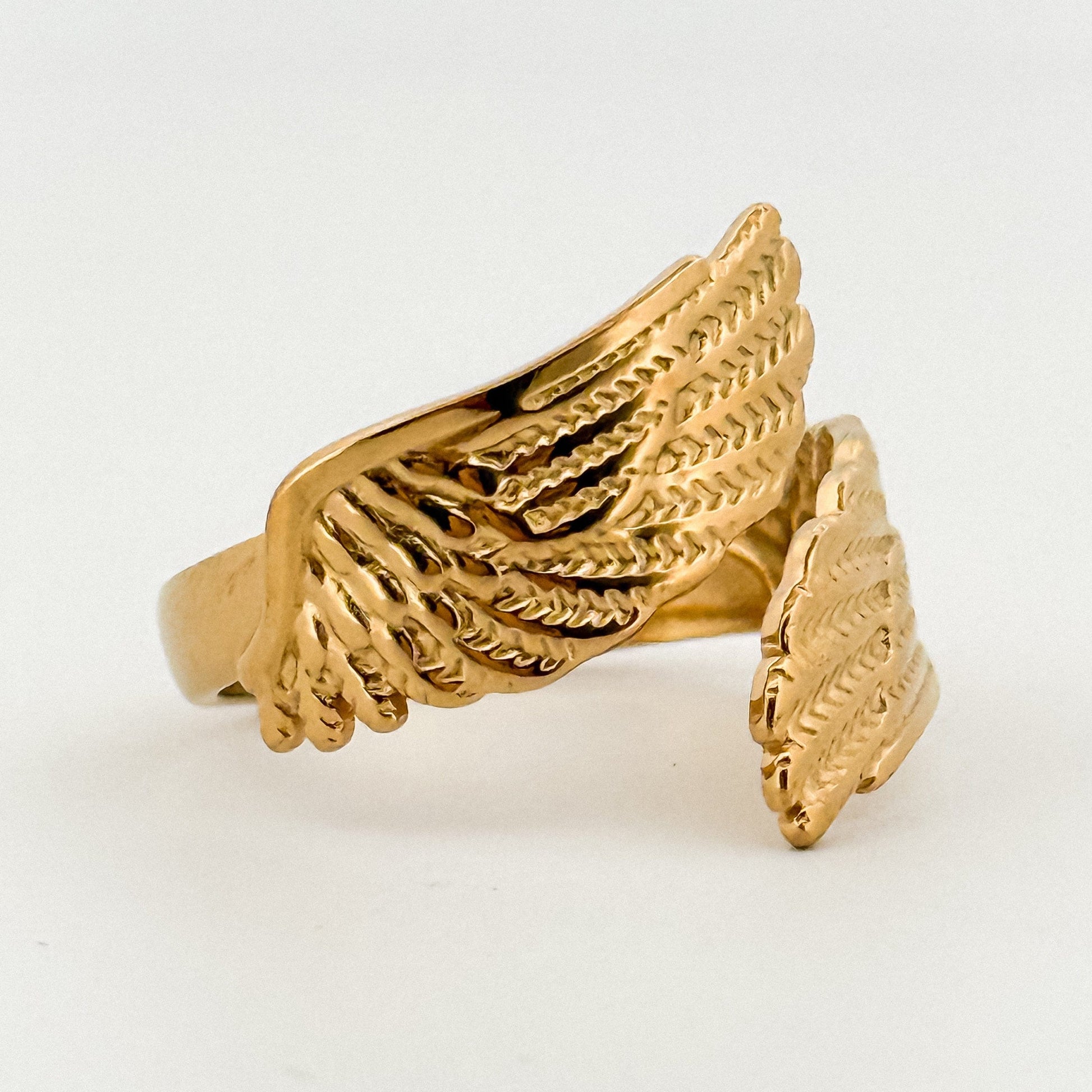 Gold wing-shaped ring on a light gray background