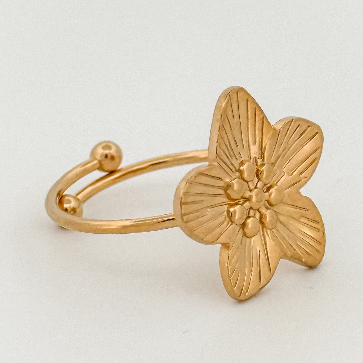 Gold flower-shaped ring on a light gray background