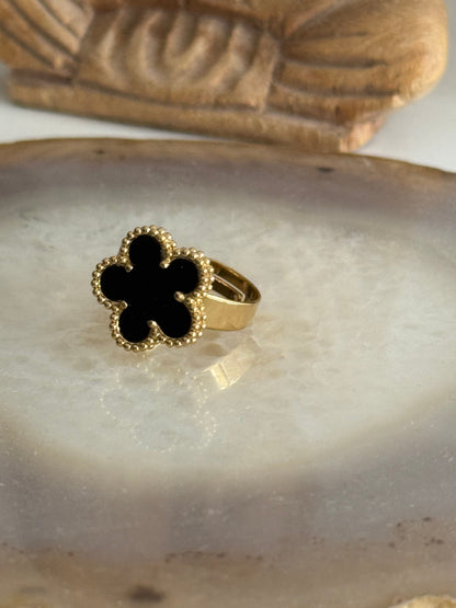 Gold ring with a black flower design on a stone surface