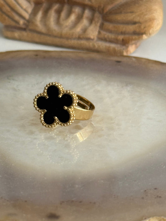 Gold ring with a black flower design on a stone surface