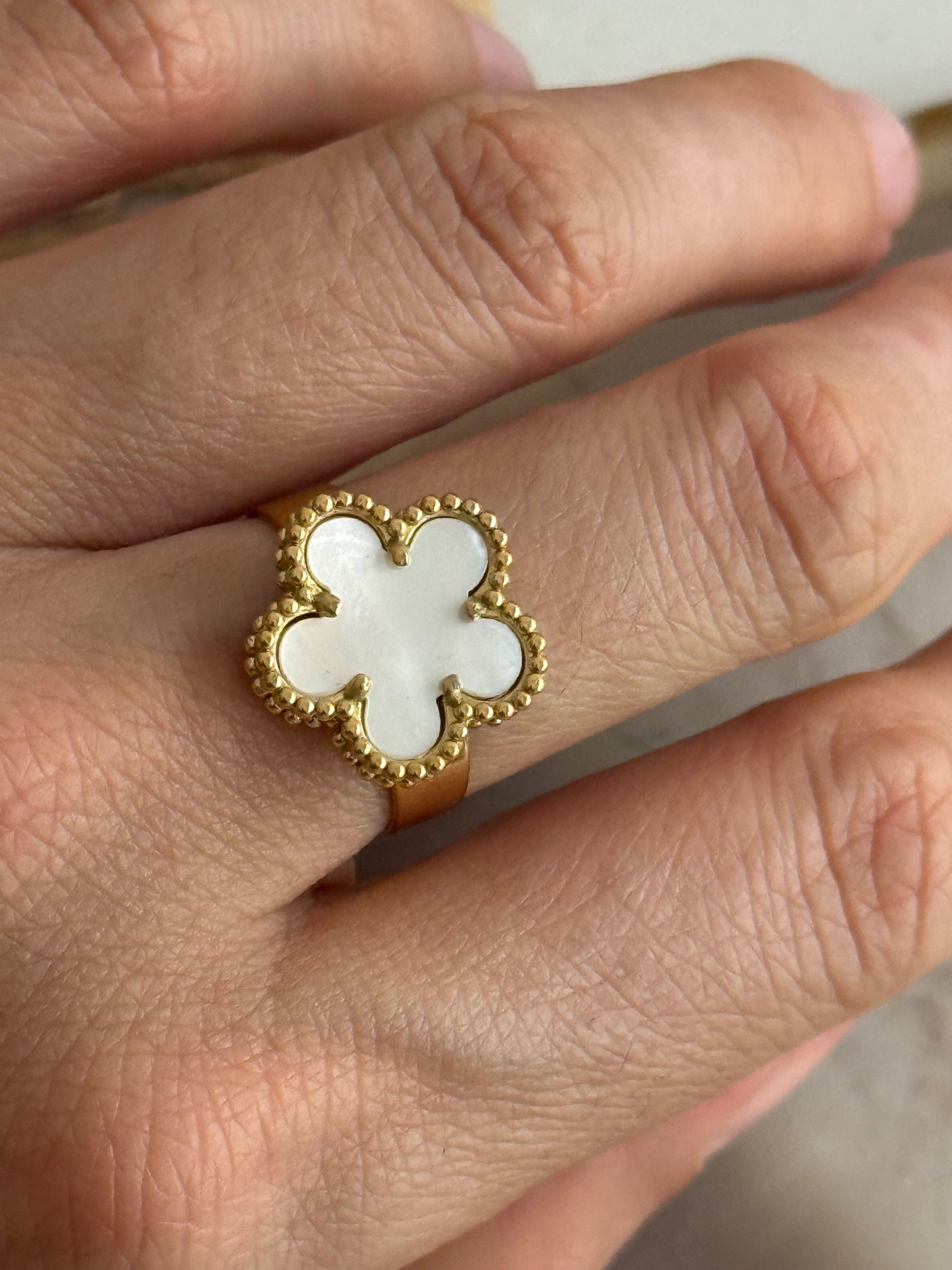 Gold flower ring with a mother pearl stone on a person's finger