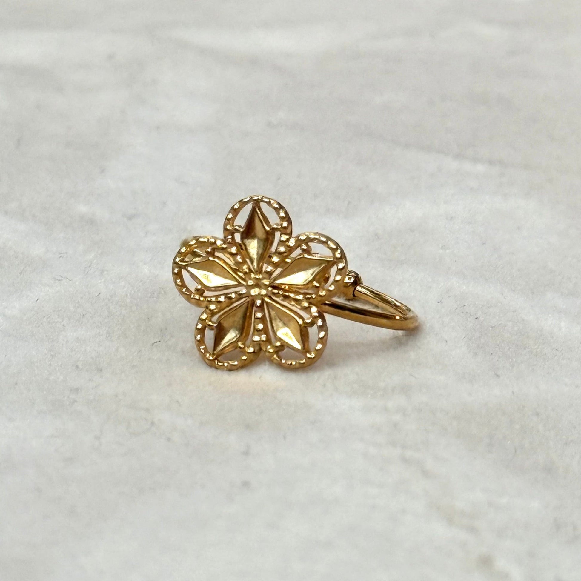 A gold-colored floral ring with a sparkling stone in the center, displayed against a marble background.