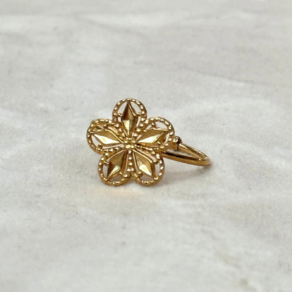 A gold-colored floral ring with a sparkling stone in the center, displayed against a marble background.