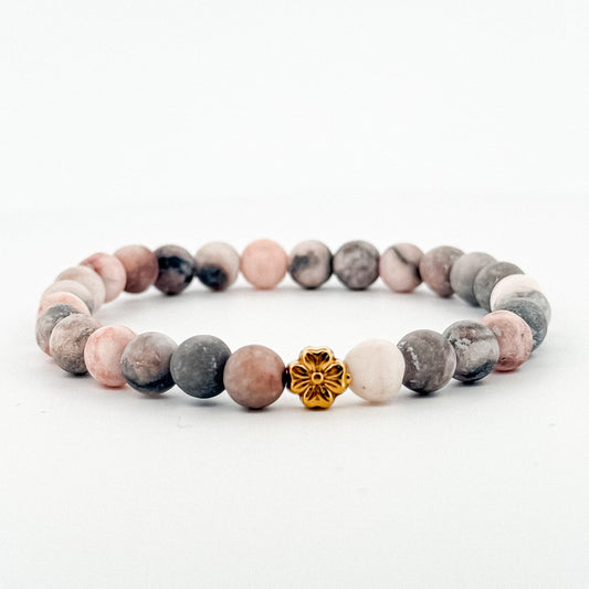 Smooth marble pink beaded bracelet with a gold flower charm on a white background