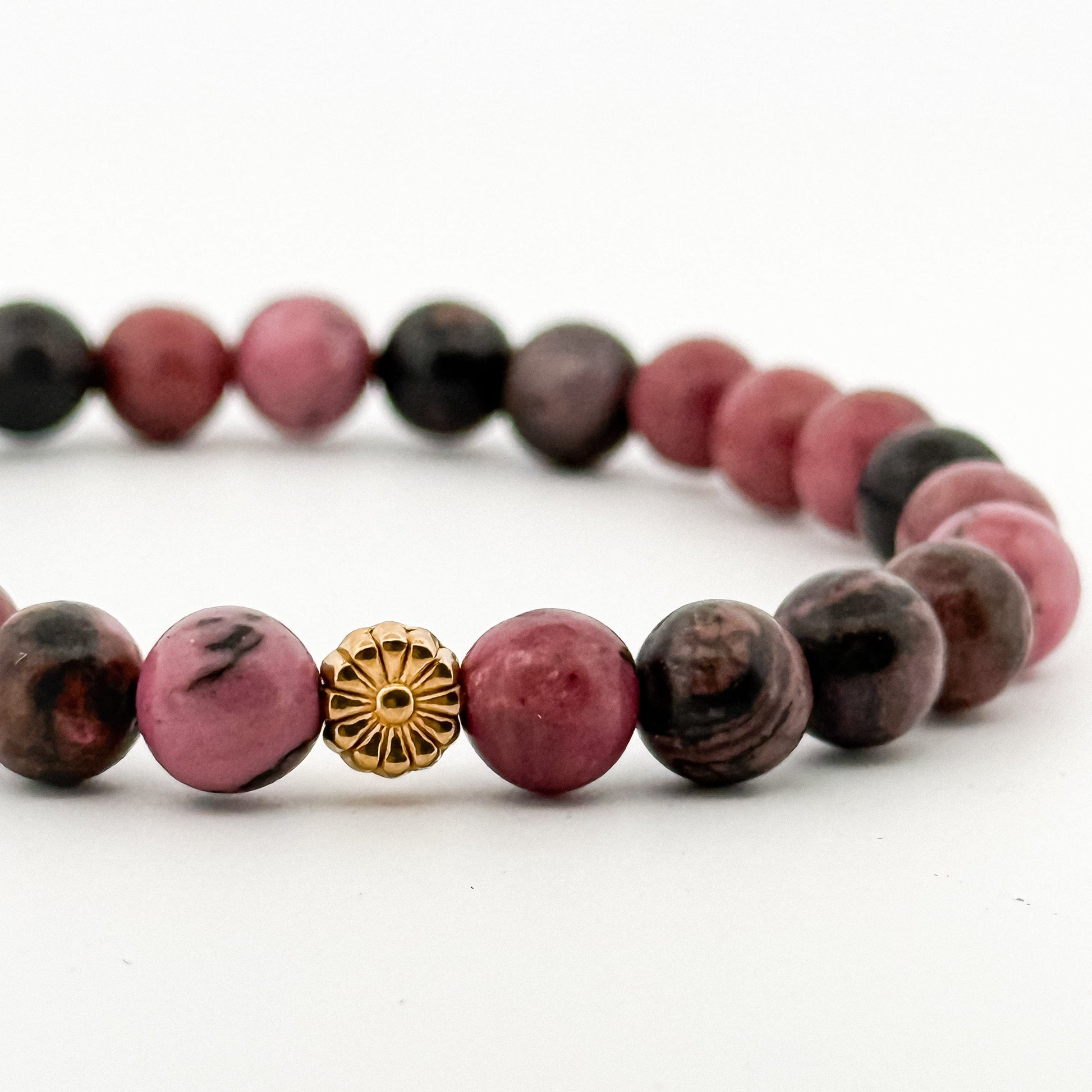 Bracelet with pink and black beads and a gold charm on a white background