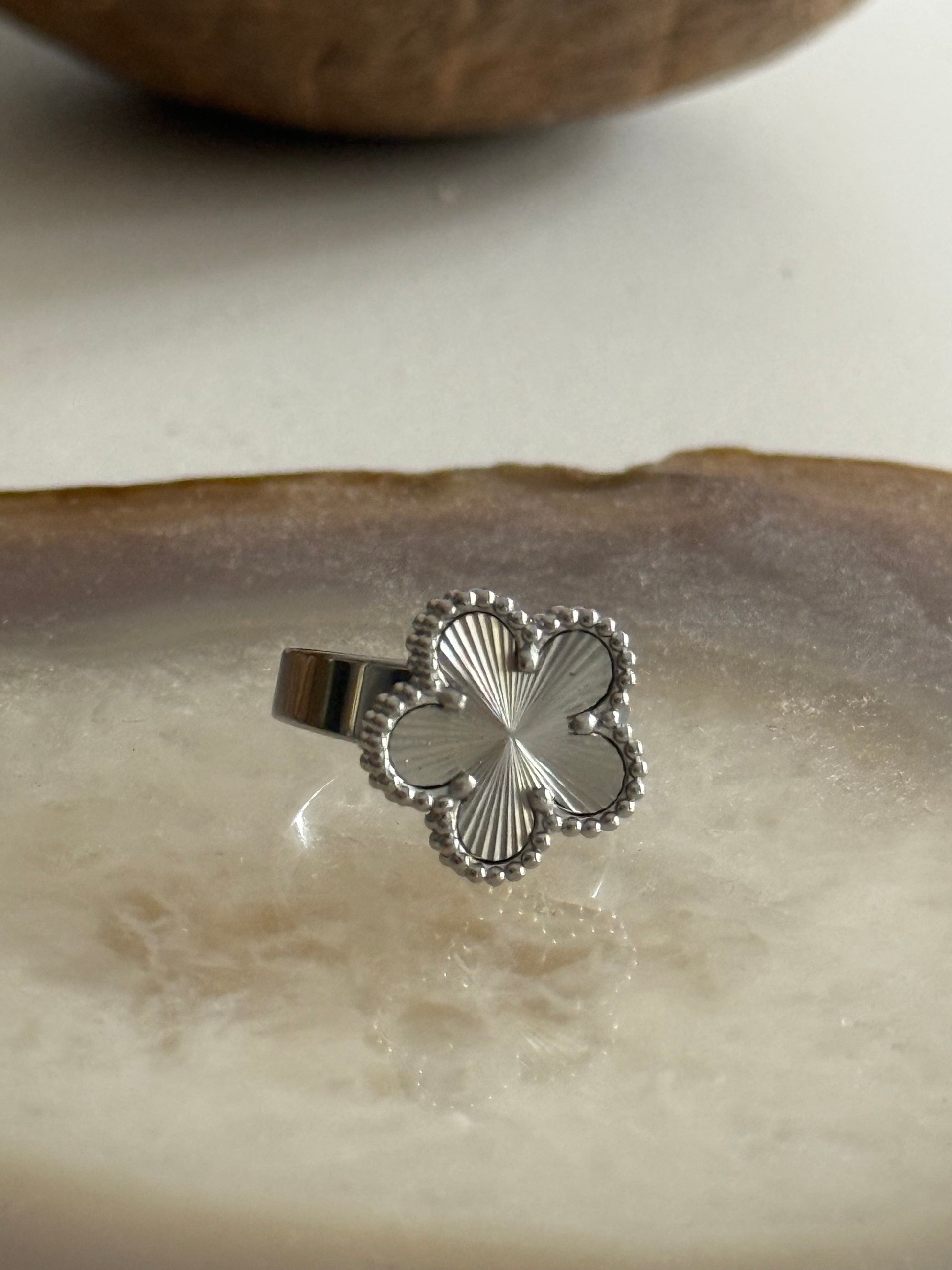 Silver four-leaf clover ring on a textured surface