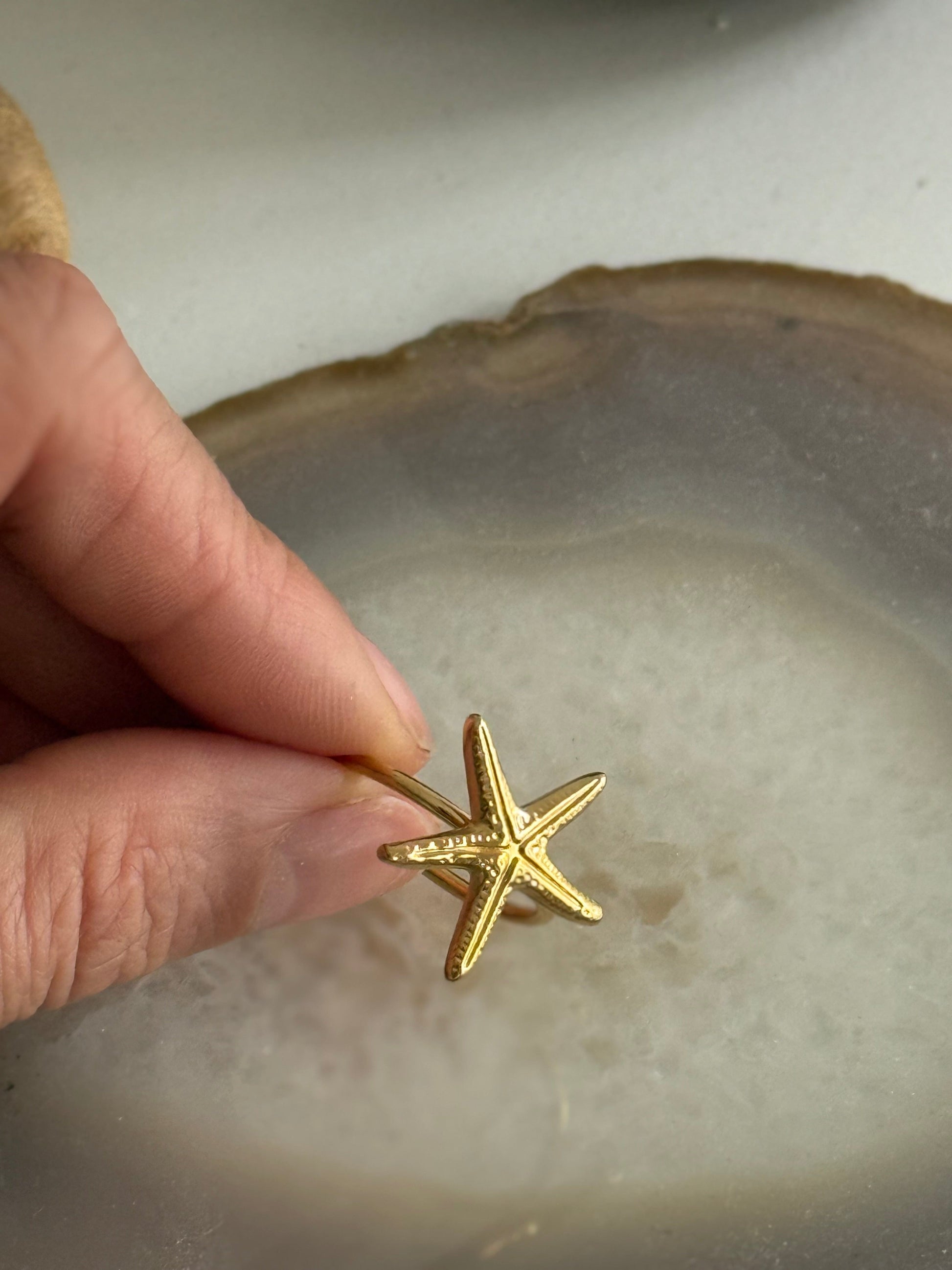 Gold starfish ring held by a hand on a textured surface